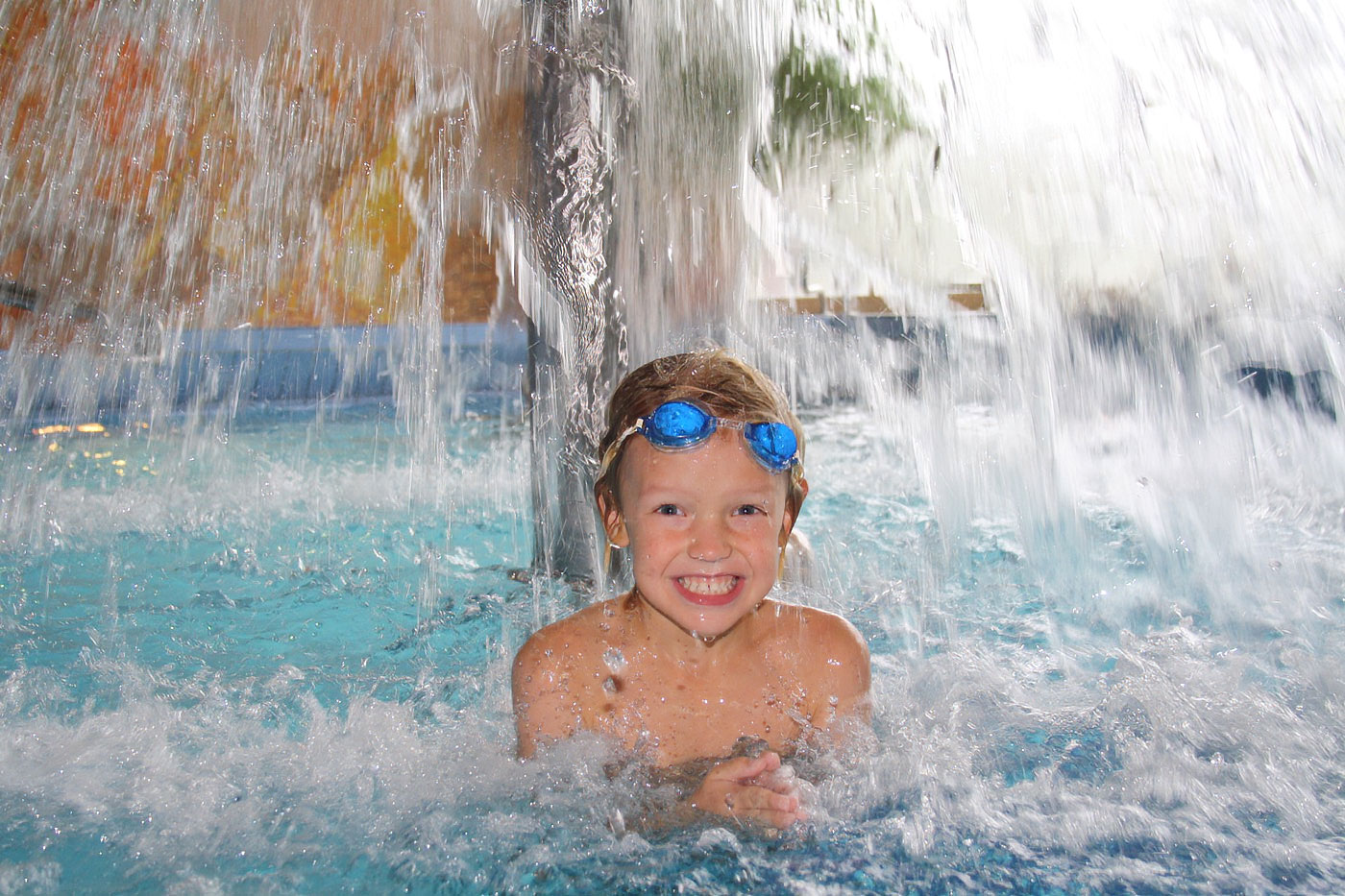 Kind sitzt unter einem Wasserpilz und wird von herabströmendem Wasser überschüttet.