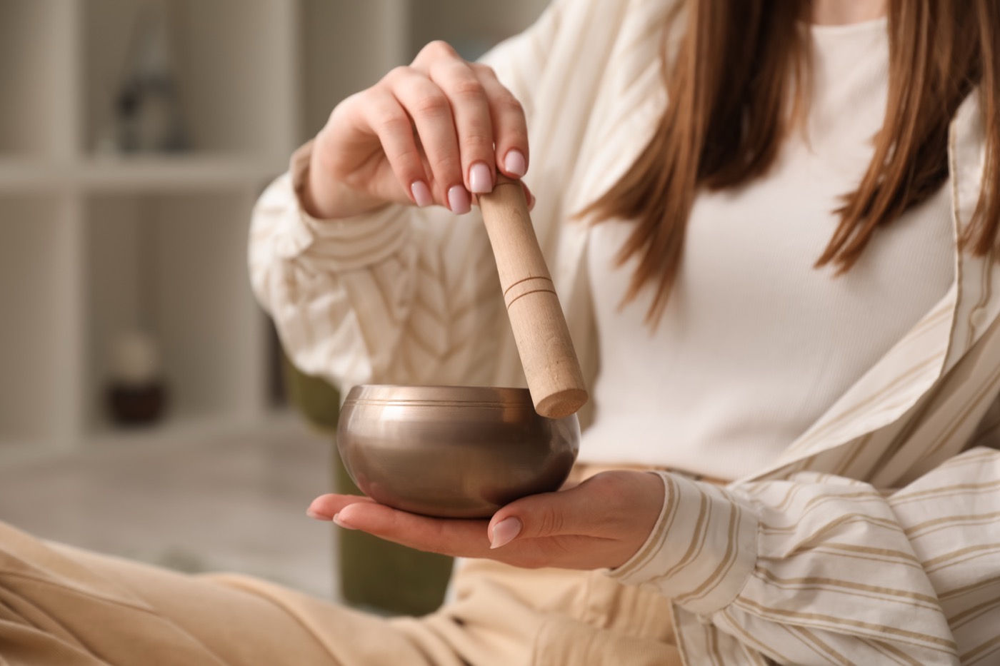 Eine Hand hält einen Holzstab und berührt mit diesem eine Klangschale die in der anderen Hand gehalten wird.